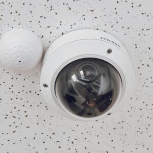 Close-up of a round dome surveillance camera installed on a speckled ceiling for security monitoring.